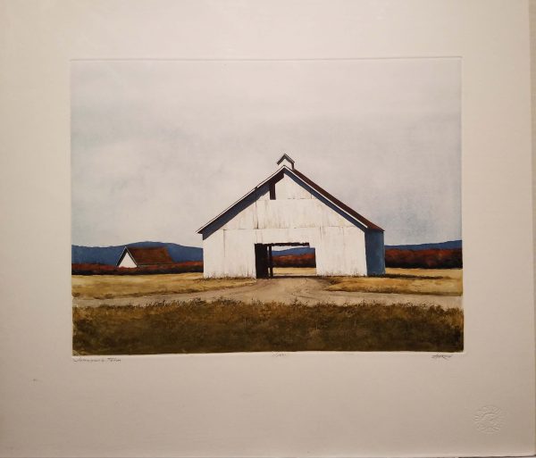 White farmhouse stands out in the tall golden grasses, gray skies and hills far away.