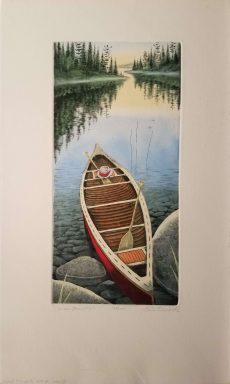 A canoe sits with one end on the rocks on the shore of a lake bordered by tall green trees.